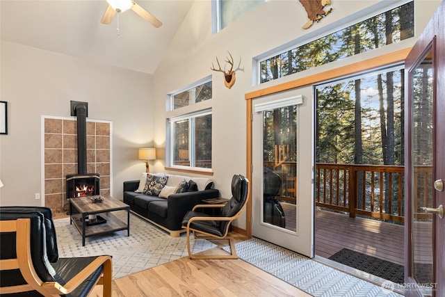 living room with ceiling fan, high vaulted ceiling, wood finished floors, and a wood stove