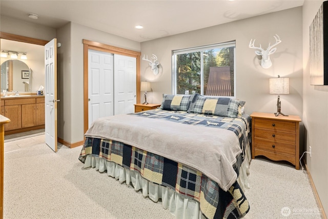 bedroom featuring arched walkways, a closet, light colored carpet, ensuite bath, and baseboards