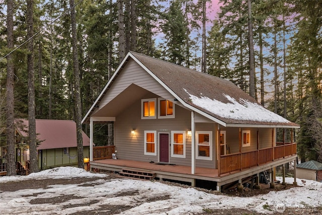 chalet / cabin with a shingled roof, a deck, and an outdoor structure