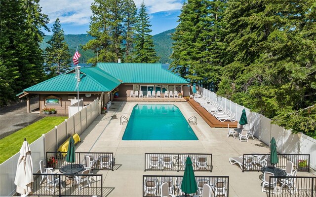 community pool featuring outdoor dining space, a patio area, a mountain view, and a fenced backyard