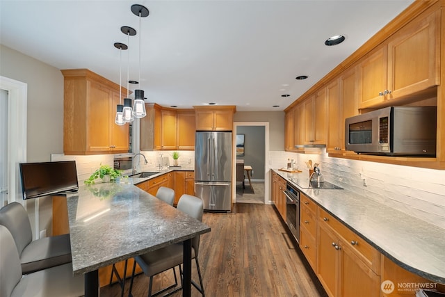 kitchen featuring appliances with stainless steel finishes, a breakfast bar area, dark wood-type flooring, decorative light fixtures, and a sink