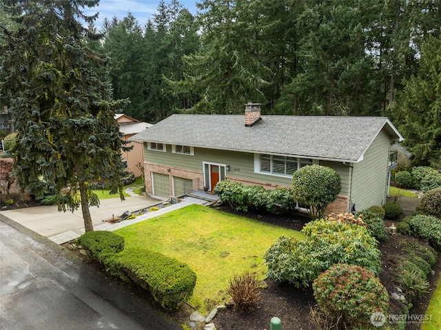 split foyer home with brick siding, a chimney, concrete driveway, an attached garage, and a front lawn