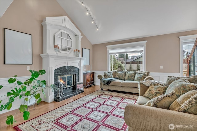 living area with a wainscoted wall, a high end fireplace, vaulted ceiling, track lighting, and wood finished floors