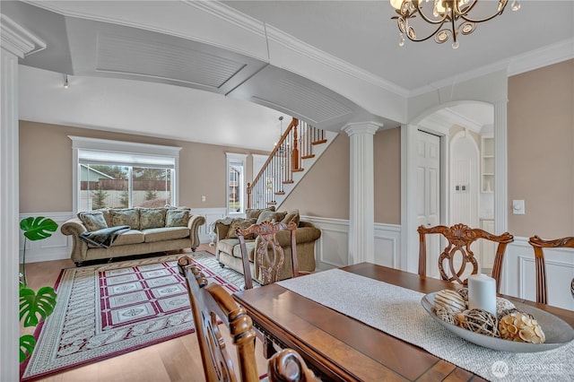 dining space featuring arched walkways, a wainscoted wall, ornate columns, and stairs