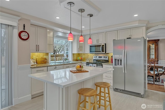 kitchen with a wainscoted wall, white cabinetry, stainless steel appliances, and backsplash