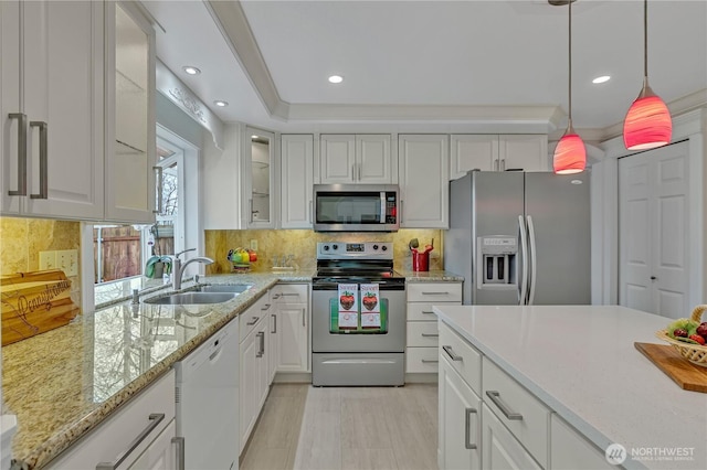 kitchen with decorative light fixtures, decorative backsplash, appliances with stainless steel finishes, white cabinets, and a sink