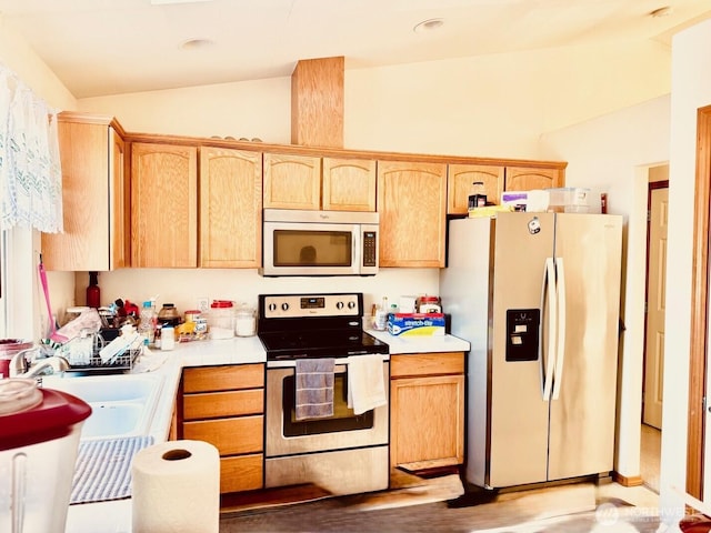 kitchen with appliances with stainless steel finishes, lofted ceiling, a sink, and light brown cabinetry