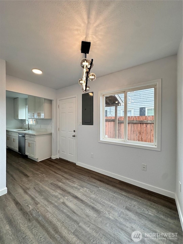 unfurnished dining area featuring a textured ceiling, a sink, baseboards, electric panel, and dark wood finished floors