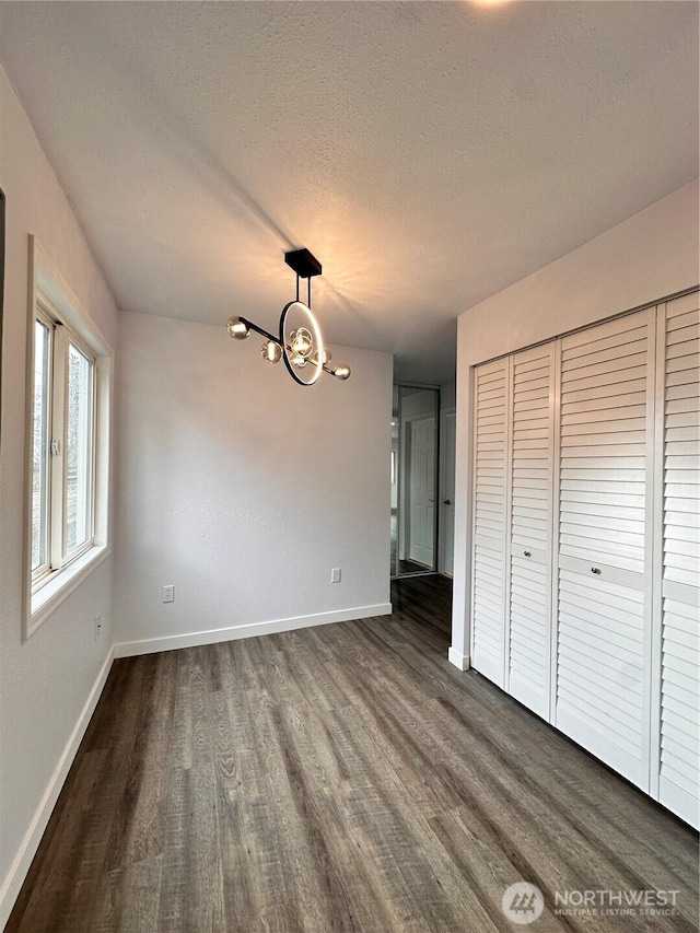 unfurnished dining area with dark wood-type flooring, a chandelier, a textured ceiling, and baseboards