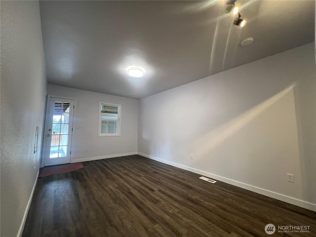 empty room featuring dark wood-style floors, visible vents, and baseboards