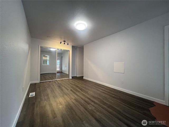 unfurnished bedroom featuring dark wood-type flooring, a closet, visible vents, and baseboards