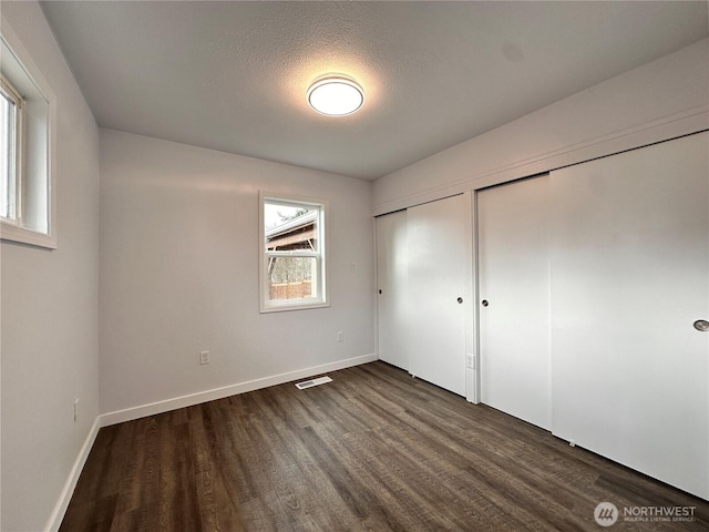 unfurnished bedroom with a textured ceiling, dark wood-type flooring, visible vents, baseboards, and multiple closets