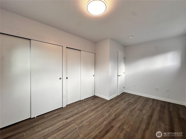 unfurnished bedroom with a textured ceiling, baseboards, dark wood finished floors, and a closet