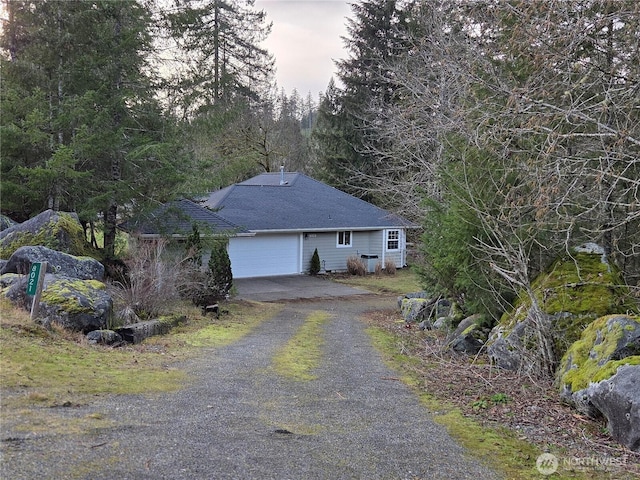 exterior space featuring gravel driveway, an attached garage, and a shingled roof