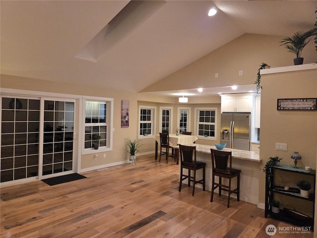 kitchen featuring stainless steel refrigerator with ice dispenser, lofted ceiling, light wood-style flooring, a peninsula, and a kitchen breakfast bar