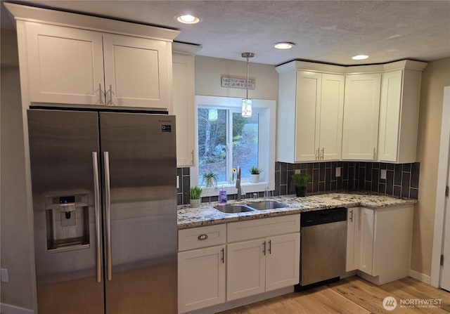 kitchen featuring stainless steel appliances, backsplash, white cabinets, a sink, and light wood-type flooring