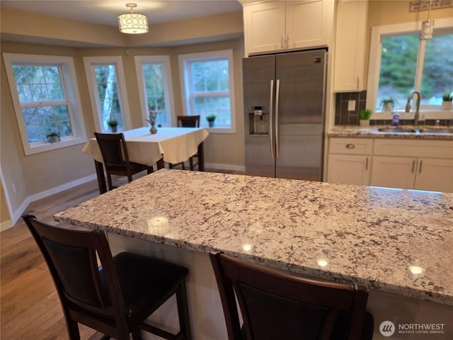 kitchen featuring wood finished floors, a sink, white cabinets, stainless steel refrigerator with ice dispenser, and light stone countertops