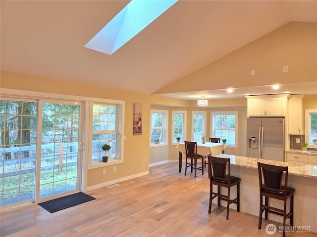 kitchen featuring visible vents, white cabinets, light stone countertops, stainless steel fridge, and a kitchen bar