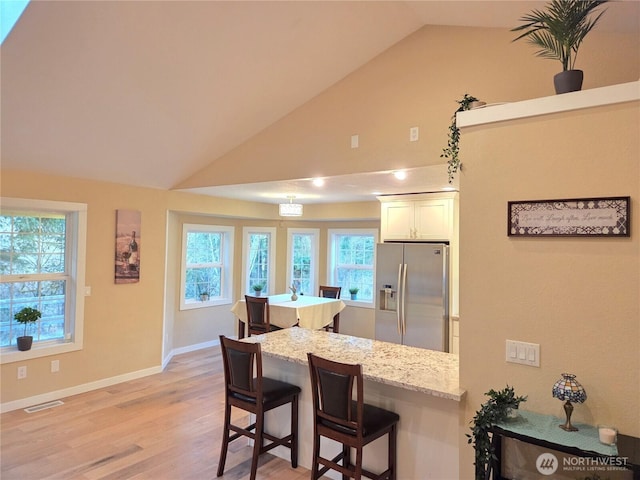 kitchen with white cabinetry, visible vents, a kitchen breakfast bar, light stone countertops, and stainless steel fridge