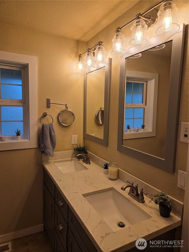 bathroom with a textured ceiling, double vanity, a sink, and visible vents