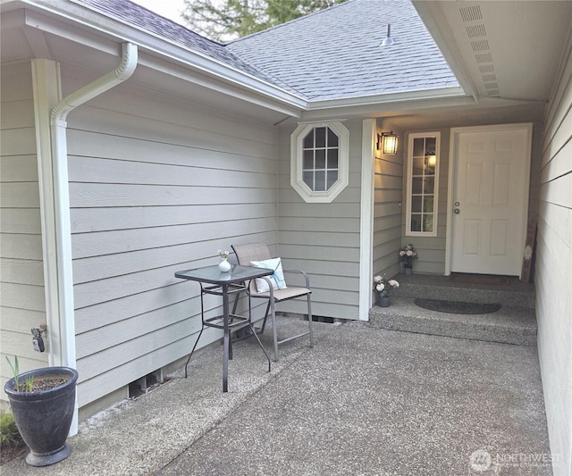 property entrance featuring a shingled roof and a patio area