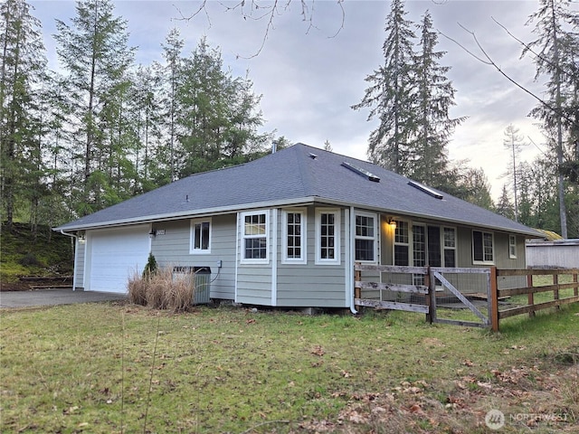 back of property featuring an attached garage, fence, driveway, a yard, and roof with shingles