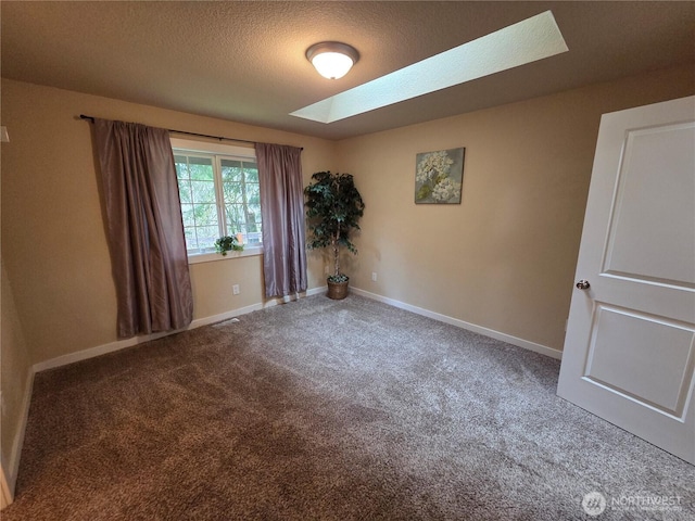 carpeted empty room with a skylight, visible vents, a textured ceiling, and baseboards