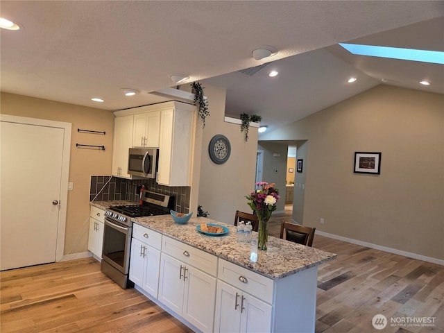 kitchen with tasteful backsplash, white cabinets, a peninsula, stainless steel appliances, and light wood-style floors