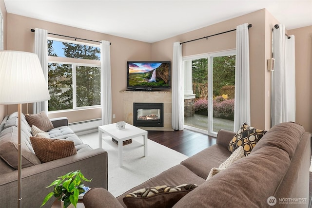 living area with a baseboard heating unit, a tile fireplace, and dark wood finished floors