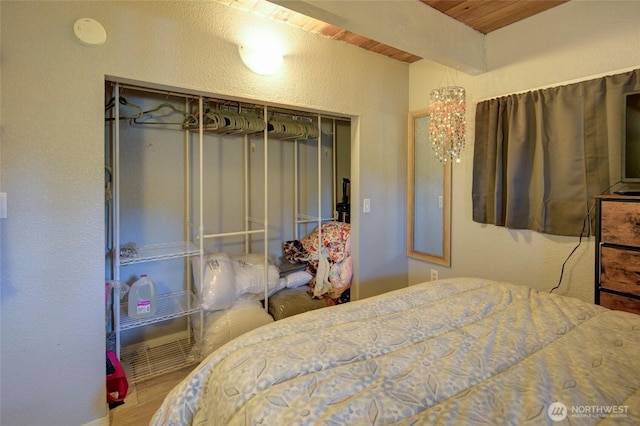 bedroom featuring a textured wall, wood finished floors, wood ceiling, a closet, and beam ceiling