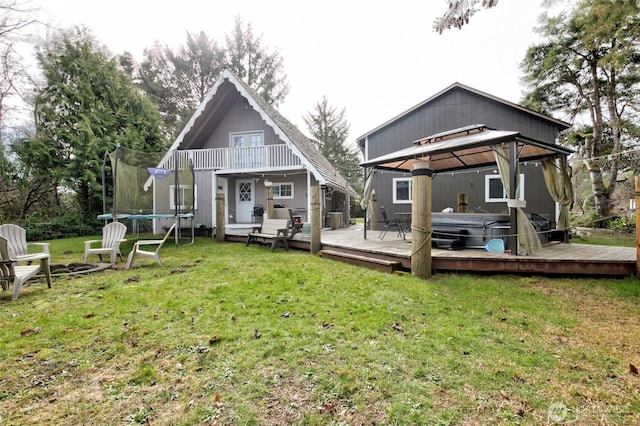 back of house with a fire pit, a gazebo, a lawn, a trampoline, and a hot tub