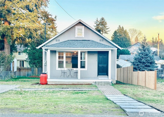 bungalow featuring roof with shingles, covered porch, a front yard, fence, and an outdoor structure