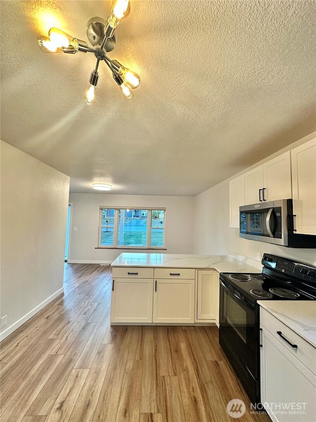 kitchen with light wood-style flooring, a peninsula, white cabinetry, black electric range oven, and stainless steel microwave