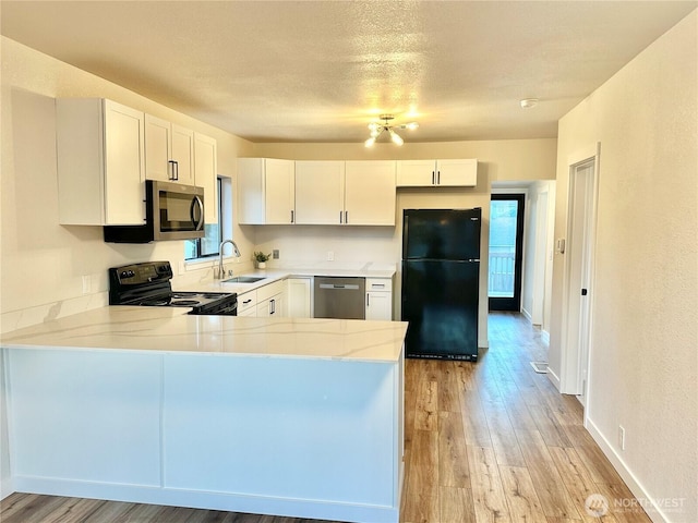 kitchen with light wood finished floors, a peninsula, black appliances, white cabinetry, and a sink