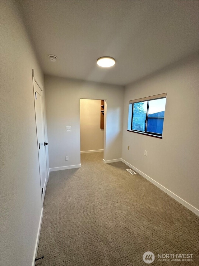 unfurnished bedroom with a closet, visible vents, a spacious closet, carpet flooring, and baseboards