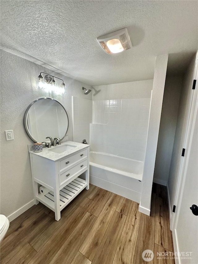 bathroom featuring shower / bathtub combination, toilet, a textured ceiling, vanity, and wood finished floors