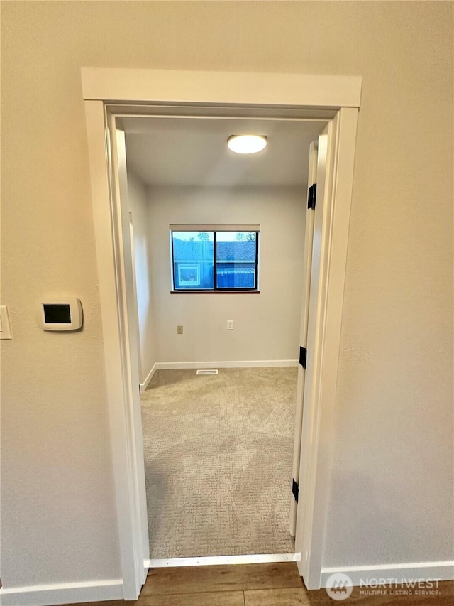 corridor with carpet floors, visible vents, and baseboards