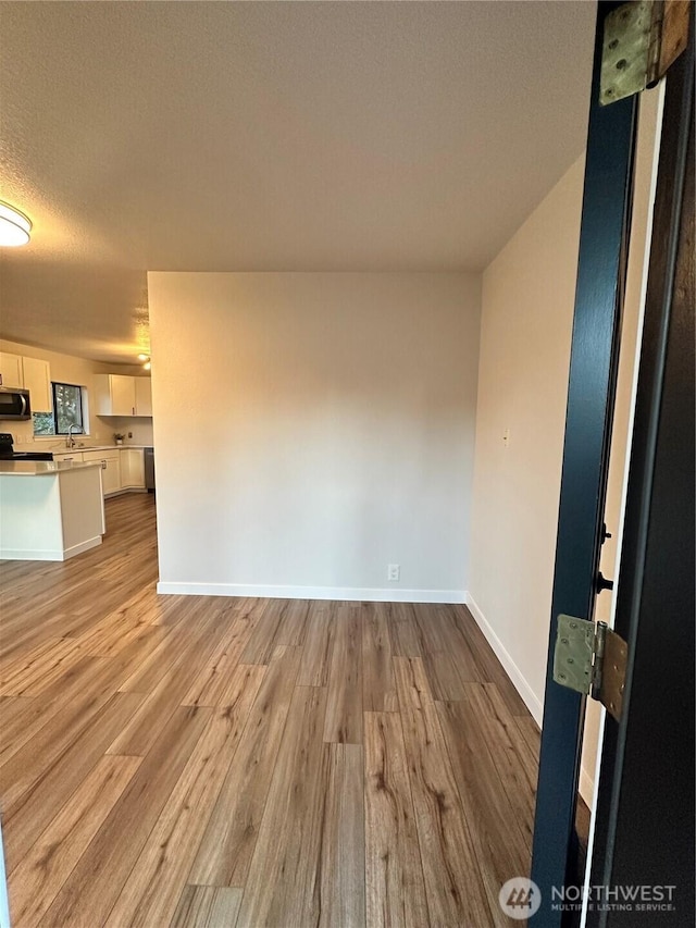 spare room with baseboards, a textured ceiling, and light wood-style floors