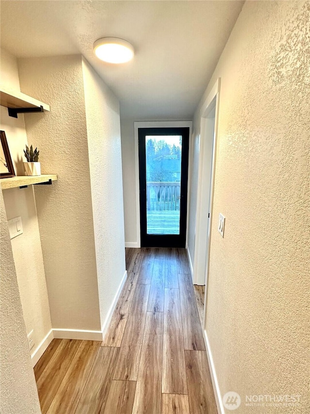 hallway featuring a textured wall, baseboards, and wood finished floors