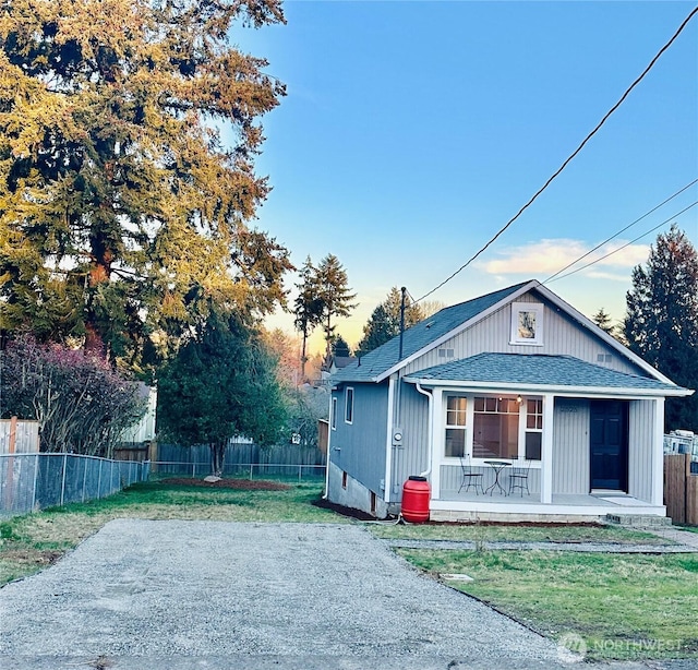 view of front of property featuring covered porch, a shingled roof, a front yard, and fence