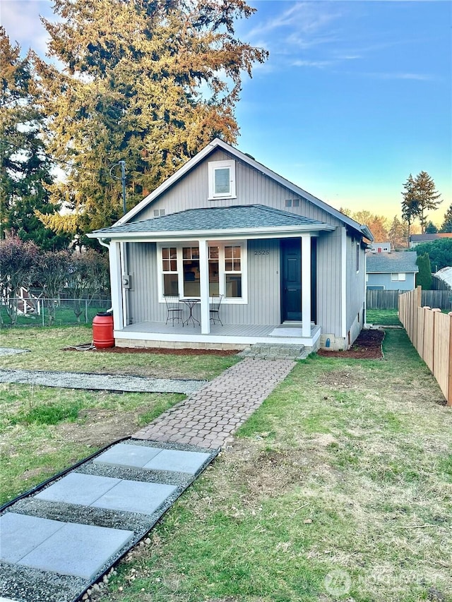 bungalow with a porch, fence, a shingled roof, and a front lawn