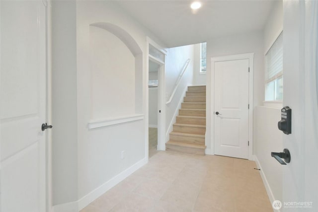 hallway featuring stairway, baseboards, and arched walkways