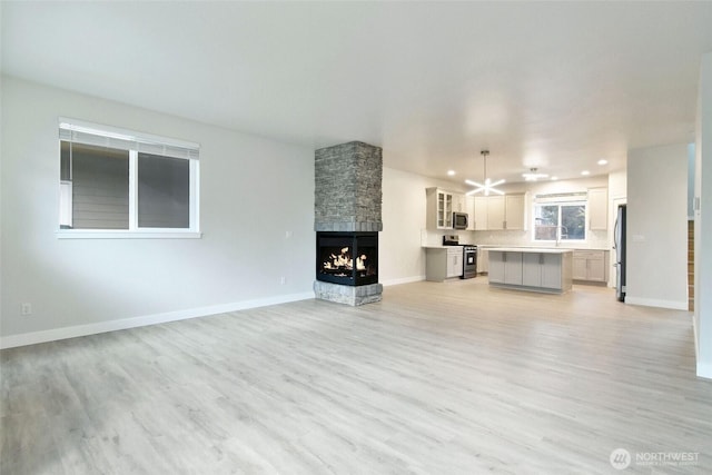 unfurnished living room with light wood-type flooring, recessed lighting, a fireplace, and baseboards