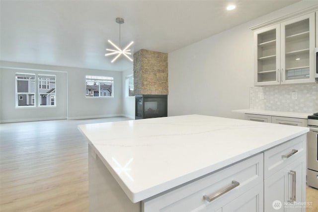 kitchen featuring a fireplace, open floor plan, a center island, tasteful backsplash, and glass insert cabinets