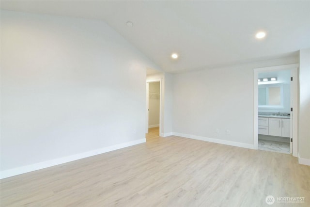 spare room with lofted ceiling, light wood-style flooring, recessed lighting, a sink, and baseboards