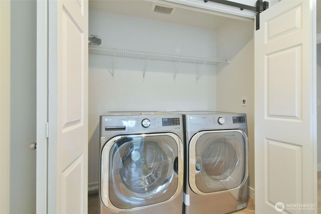 laundry room featuring laundry area, a barn door, washing machine and dryer, and visible vents