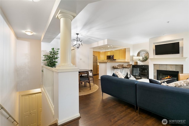 living room featuring ornate columns, dark wood-style flooring, and a tile fireplace