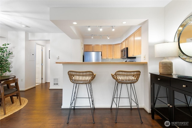 kitchen featuring appliances with stainless steel finishes, a breakfast bar, dark wood finished floors, and visible vents