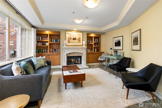 living room with crown molding, a tray ceiling, built in features, and a glass covered fireplace