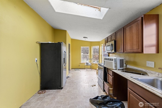 kitchen with a skylight, appliances with stainless steel finishes, light countertops, a textured ceiling, and a sink